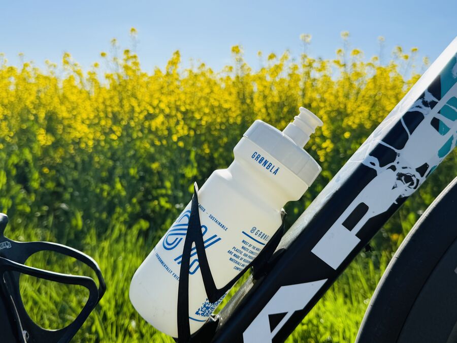 GRØNBLÅ compostable cycling water bottle in a bike cage with a yellow rapeseed field behind